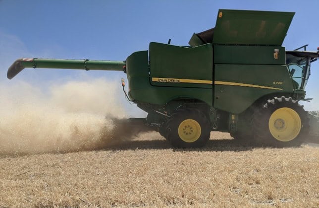 A green John Deere agricultural sprayer applying herbicide to a crop field for weed control, showcasing advanced weed science technology in farming.