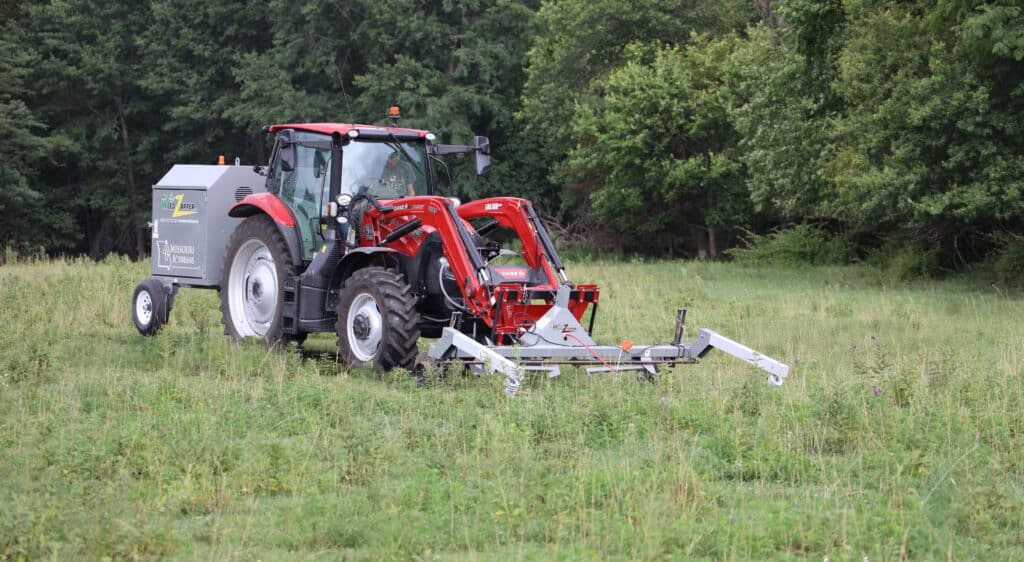 A tractor with specialized weed control machinery working in a field of wild grasses and weeds, highlighting weed science and herbicide application techniques.