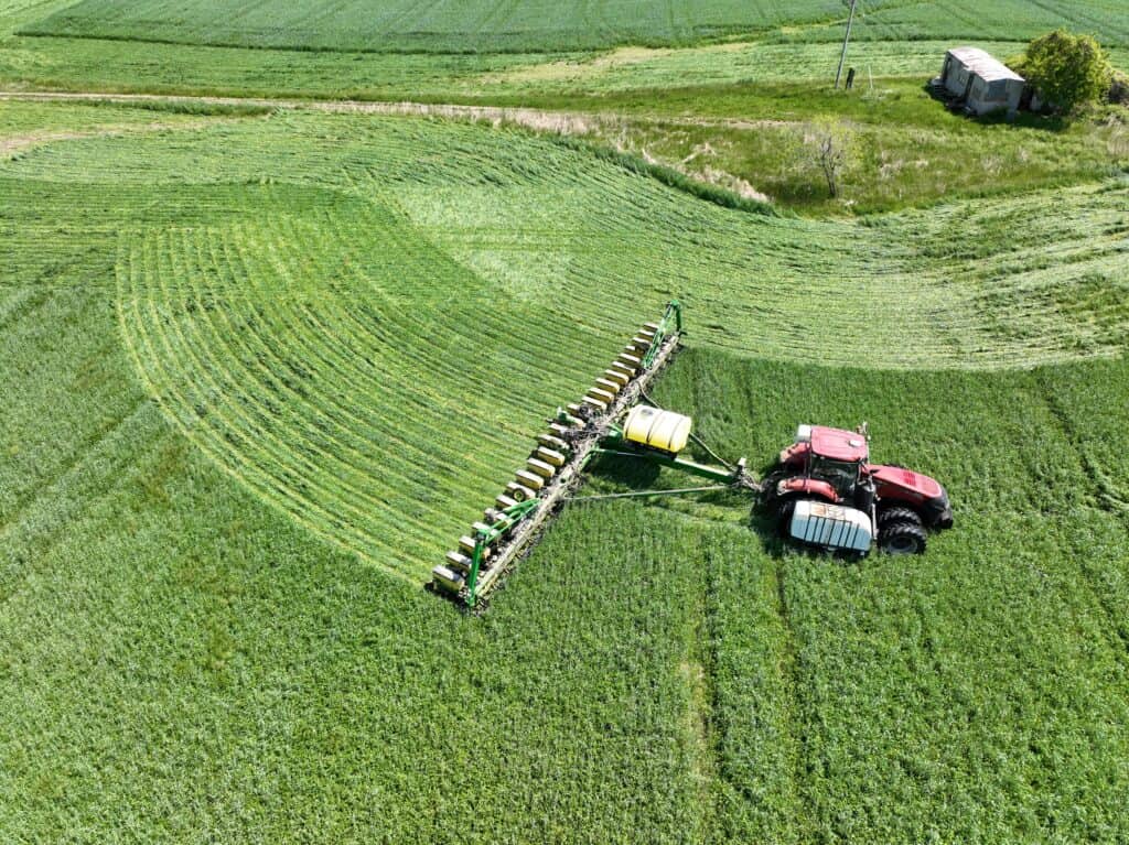Aerial view of a tractor spraying crops to control weeds in a lush green field, showcasing advanced weed science and sustainable pest management practices.