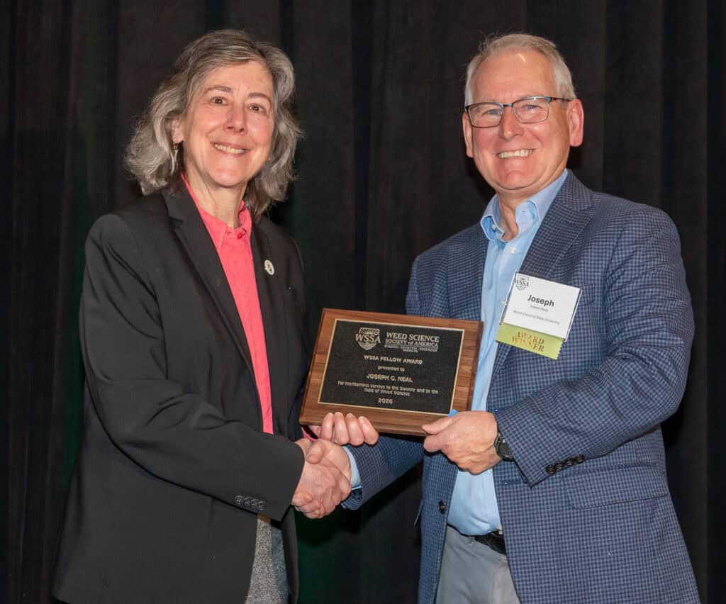 Two professionals at the Weed Science Society of America event, one presenting an award to the other, highlighting achievements in weed science research and education.