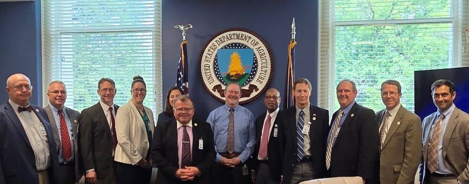 Group photo of Weed Science Society of America members in a conference room with official seal and flags, showcasing collaboration among weed science professionals.